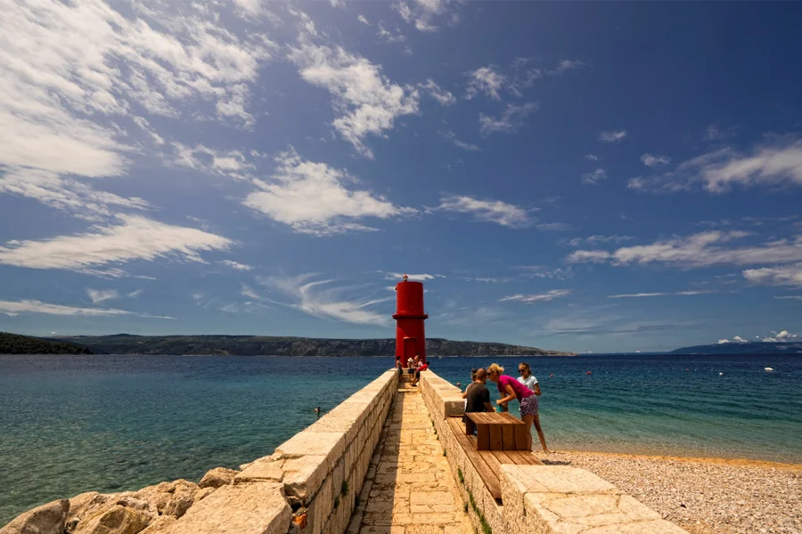 Šljunčana plaža i crveni svjetionik na Cresu
